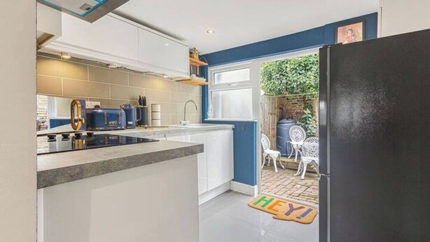 A modern kitchen with white cabinets, a black refrigerator, and a small dining area with white chairs. - OnSiteStays - Rose Cottage: Cozy Lewes Getaway (Barcombe)