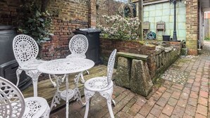 A patio with white metal chairs and a table, brick walls, and a brick building in the background. - OnSiteStays - Rose Cottage: Cozy Lewes Getaway (Barcombe)