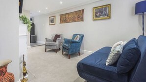 A living room with a blue sofa, a grey armchair, and a blue armchair with a cushion. There are two framed pictures on the wall. - OnSiteStays - Rose Cottage: Cozy Lewes Getaway (Barcombe)
