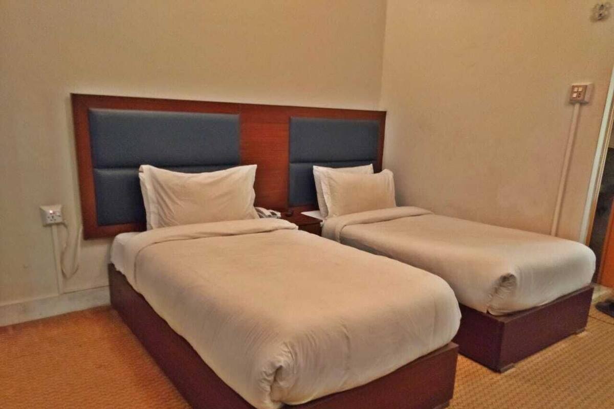 Una habitación de hotel con dos camas individuales, un cabecero de madera y suelo alfombrado.
