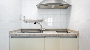 A kitchen with white tiled walls, a stainless steel sink, and a built-in range hood. - Pohang In The Blue Spa Pension (Pohang)