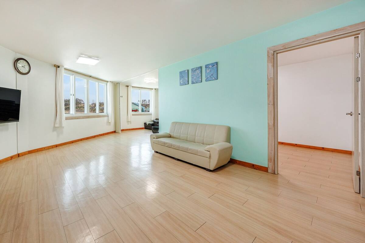 A spacious living room with a flat-screen TV, a beige sofa, and a large window offering a view of the outside.