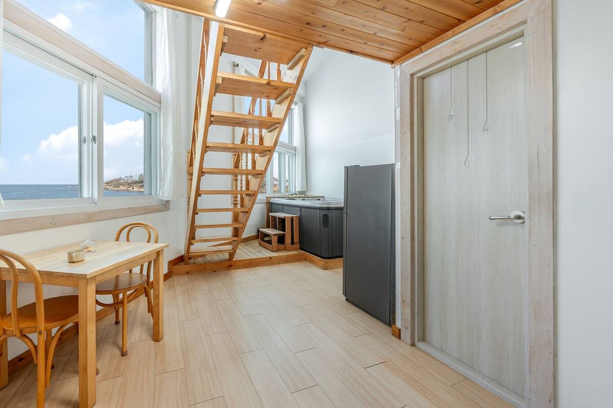 A compact kitchen with a wooden table and chairs, a built-in stove, and a view of the sea through large windows.