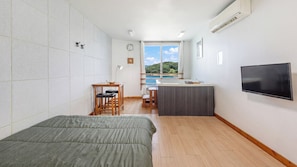 A compact hotel room with a bed, a small desk, a TV, and a view of the sea. - Pohang In The Blue Spa Pension (Pohang)