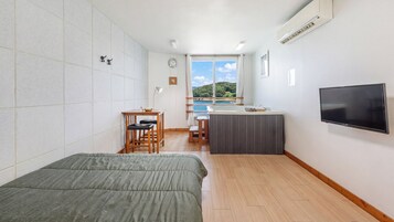 A compact hotel room with a bed, a small desk, a TV, and a view of the sea.