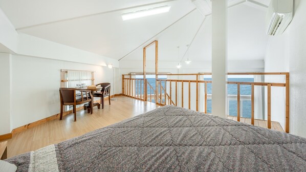 Relax in a spacious room with a large bed, wooden desk, and mirror, offering a view of the sea.