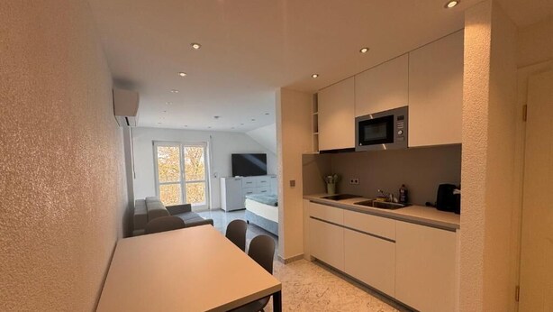 Ett modernt kök med inbyggda vitvaror, en matplats med bord och stolar samt utsikt över ett vardagsrum med soffa och tv.