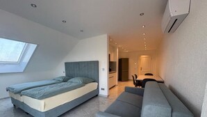 Ett modernt sovrum med en säng, en soffa, ett takfönster och ett köksområde i bakgrunden.