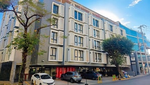 Un hotel de varios pisos con fachada moderna, amplias ventanas y un estacionamiento con varios automóviles.