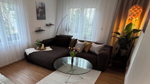 A modern living room with a dark brown sofa, a glass coffee table with a vase of flowers, and a ceiling light fixture. - Black Forest vacation apartment with dream terrace (Freudenstadt)