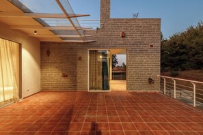 Un patio amplio con suelo de baldosas, una puerta de cristal que da a un espacio interior y un muro de ladrillo.