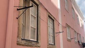 Ein pinkfarbenes Gebäude mit mehreren Fenstern, von denen einige mit Gitter versehen sind, und einer sichtbaren Tür.