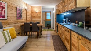 Una cocina compacta con armarios de madera, un comedor con sofá y sillas, y un ventanal.