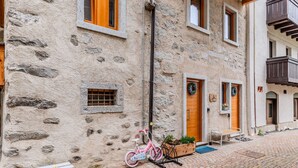 Un edificio de piedra con contraventanas de madera, una bicicleta y un banco en el exterior.