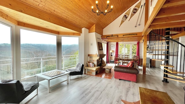 Un salón espacioso con chimenea, un ventanal grande con vistas panorámicas y una escalera de madera.
