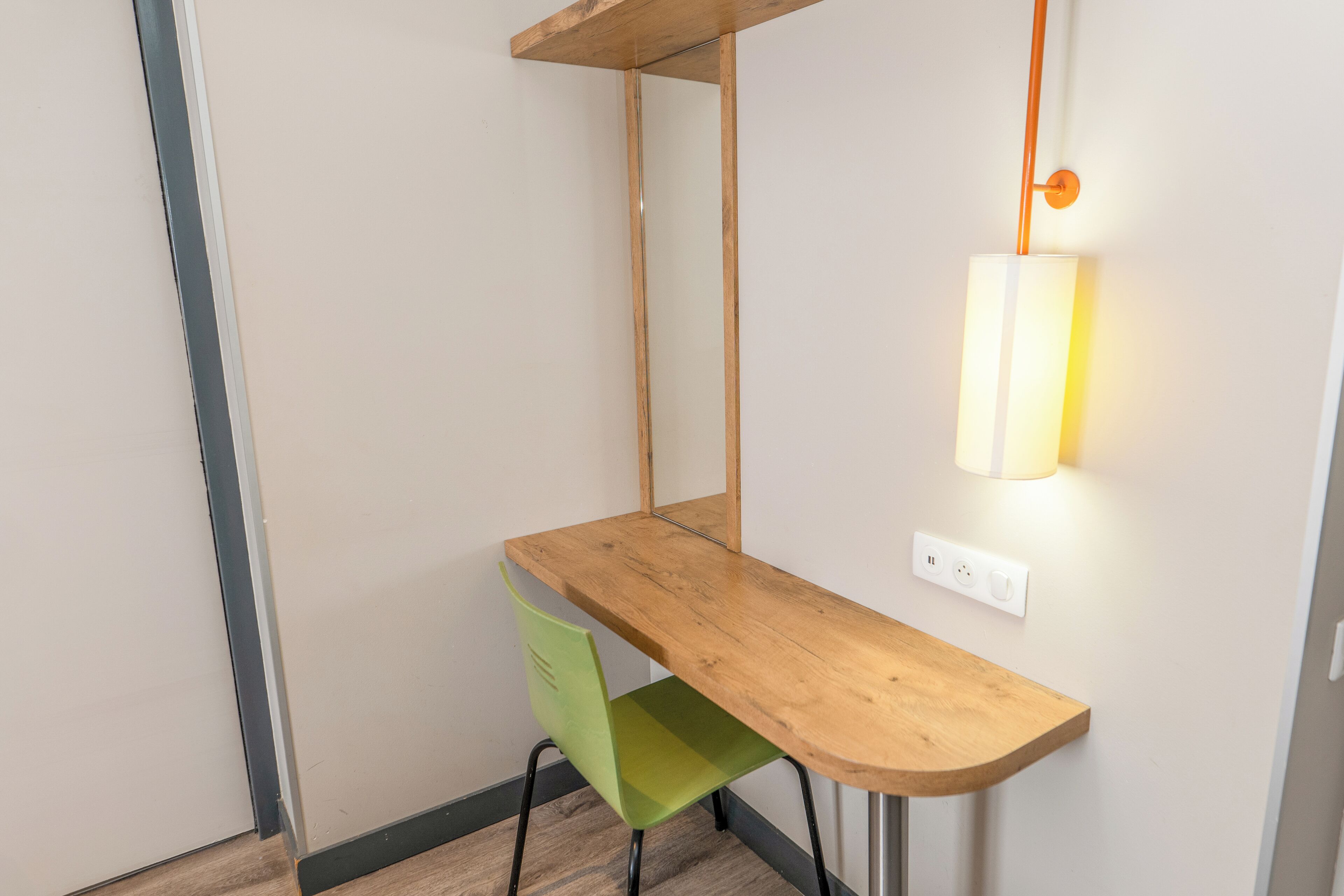 Een hoekbureau met een groene stoel, een houten plank erboven en een wandlamp.