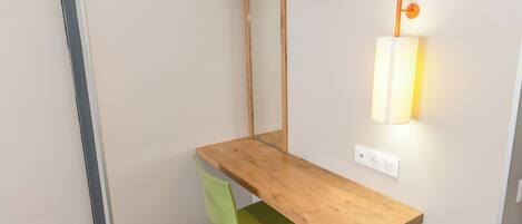 A corner desk with a green chair, a wooden shelf above, and a wall-mounted lamp.