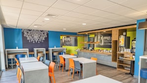 A modern cafeteria with multiple tables and chairs, a counter with food items, and a decorative wall. - Ibis Budget Brest Sud Plougastel - Hôtel Rénové (Plougastel-Daoulas)