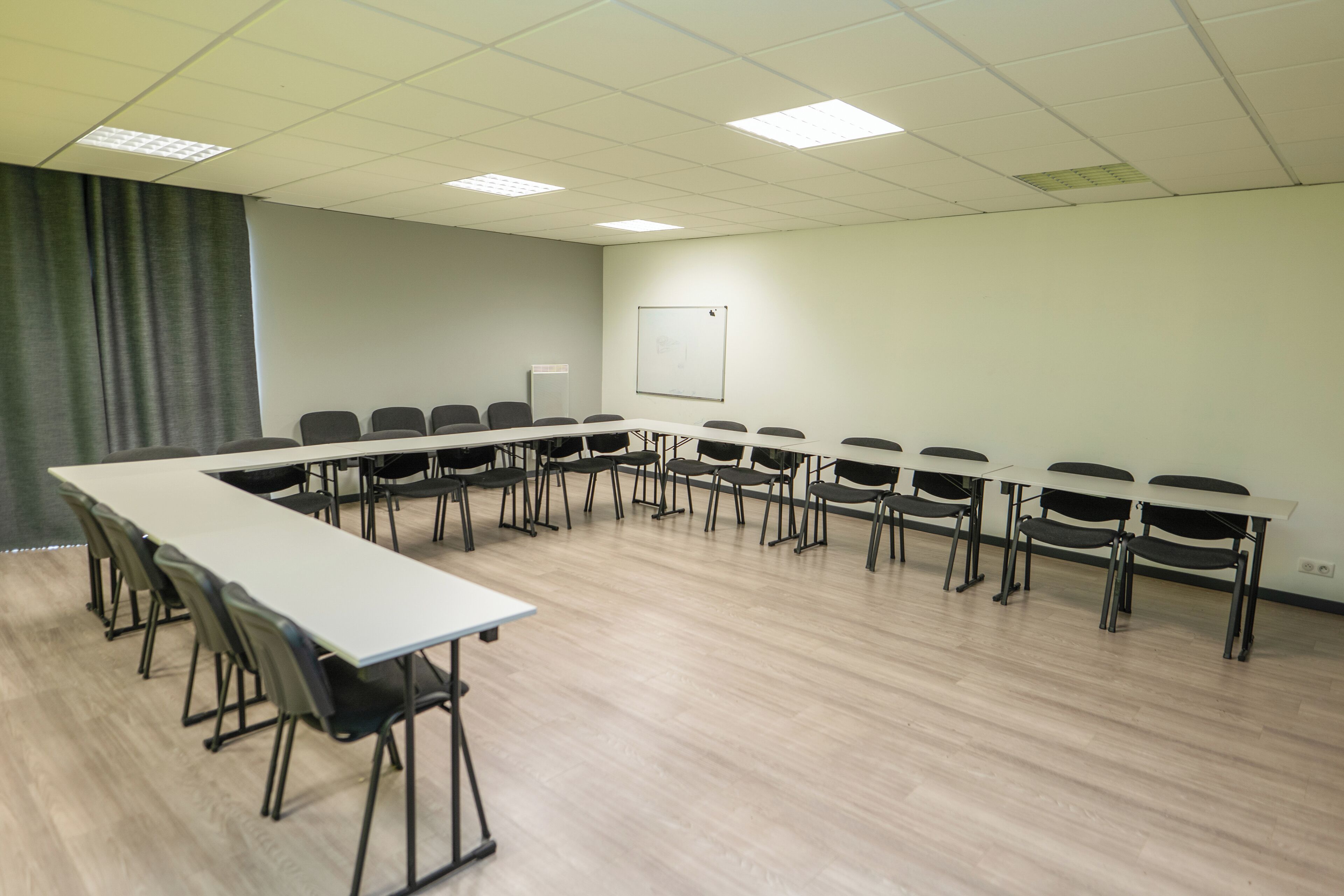 A conference room with a long table and chairs, a whiteboard, and a curtain.