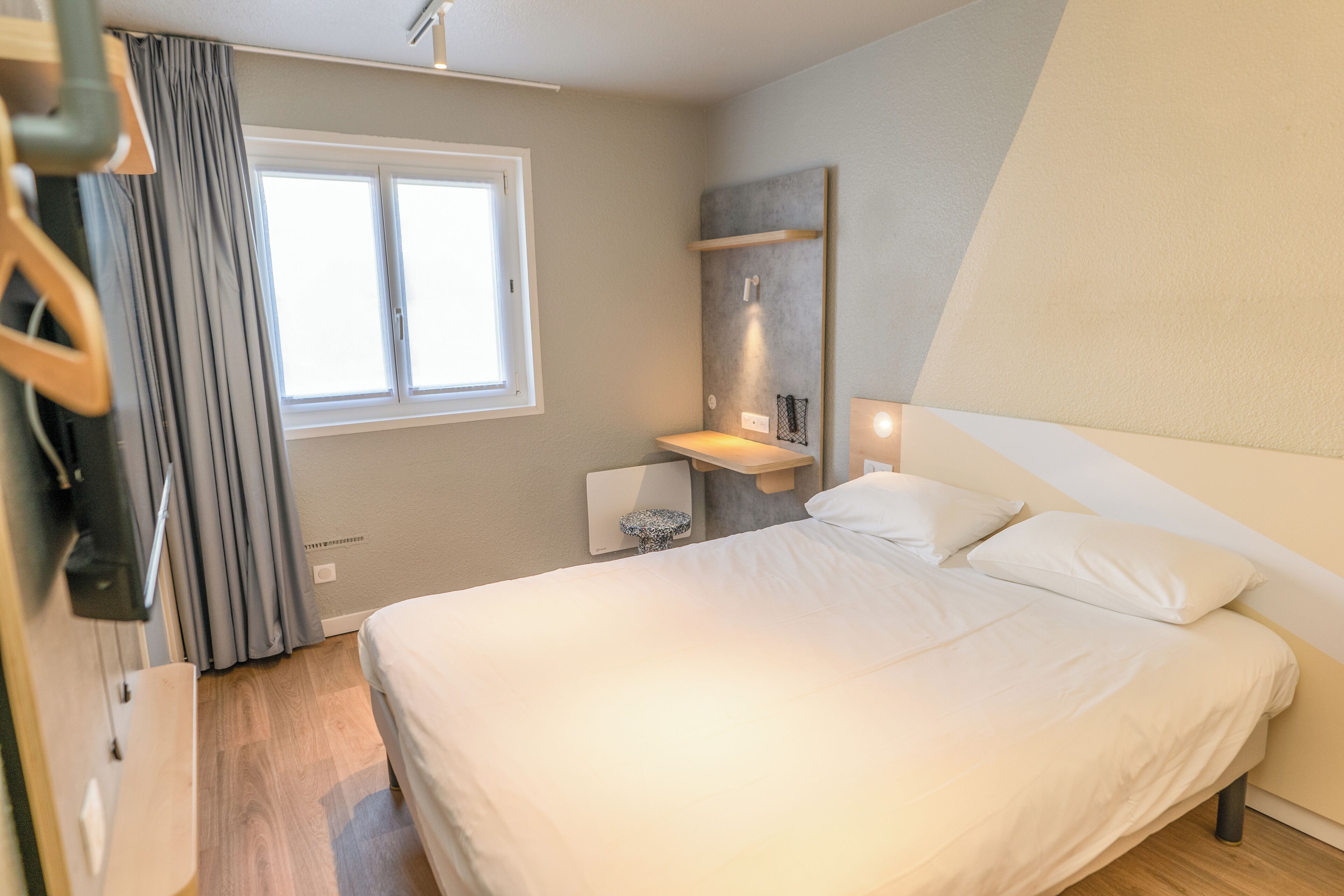 Een slaapkamer met een groot bed, een raam met gordijnen, een nachtkastje en een wandplank.