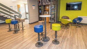 A modern interior with a wooden floor, a staircase, a vending machine, and colorful stools. - Ibis Budget Brest Sud Plougastel - Hôtel Rénové (Plougastel-Daoulas)