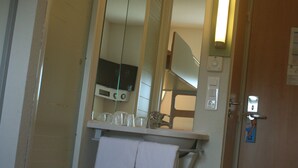 Een hotelkamer met een bed, nachtkastje, spiegel en deur.