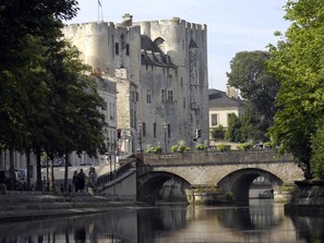 Eine Steinsche Brücke über einem ruhigen Fluss, im Hintergrund ein historisches Schloss und Fußgänger auf der Brücke.