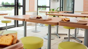 Een moderne eetruimte met tafels, stoelen en een televisiescherm.