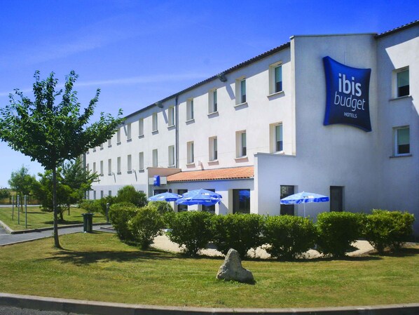 Egy épület, amelyen az ibis budget szállodalánc táblája látható, és amelyet gondosan ápolt fű és bokrok vesznek körül.