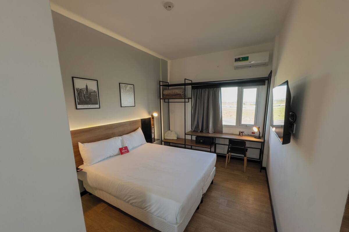 Une chambre d’hôtel avec un lit, un bureau, une chaise et un téléviseur.
