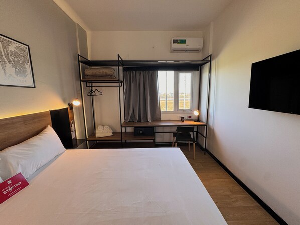 A hotel room with a bunk bed, a desk with a chair, a flat-screen TV, and a window with curtains.