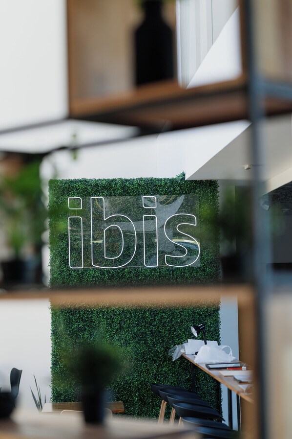 Een modern interieur met een bordje met de tekst 'ibis' op een groene muur, een bureau met een lamp en een stoel.