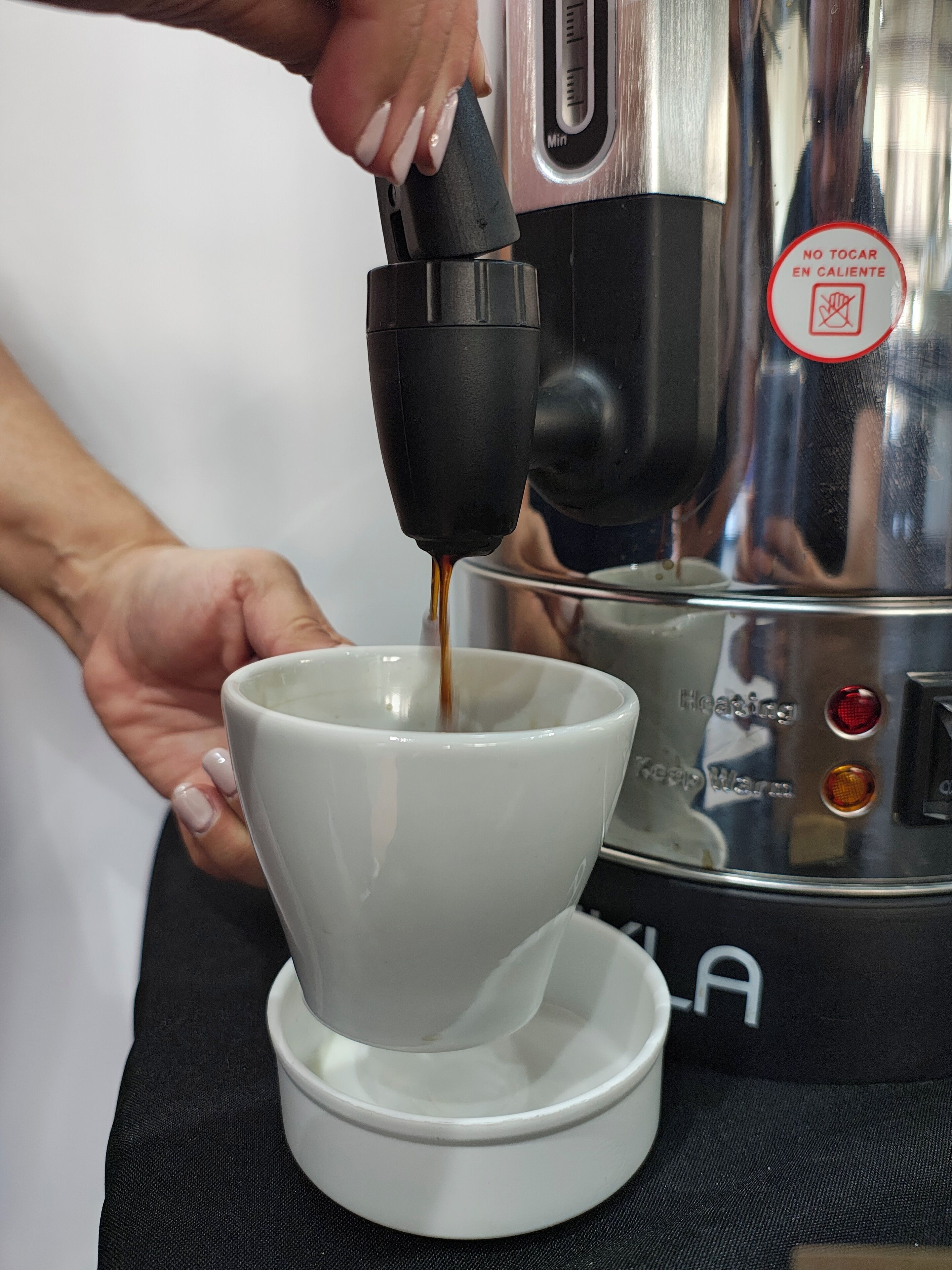 A person pouring coffee into a white cup using a coffee machine.