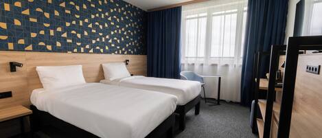 A hotel room with two beds, a small table, and a chair.