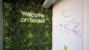 Un mur agrémenté d’un jardin vertical et d’un panneau lumineux néon sur lequel on peut lire : « Bienvenue à bord ! ».