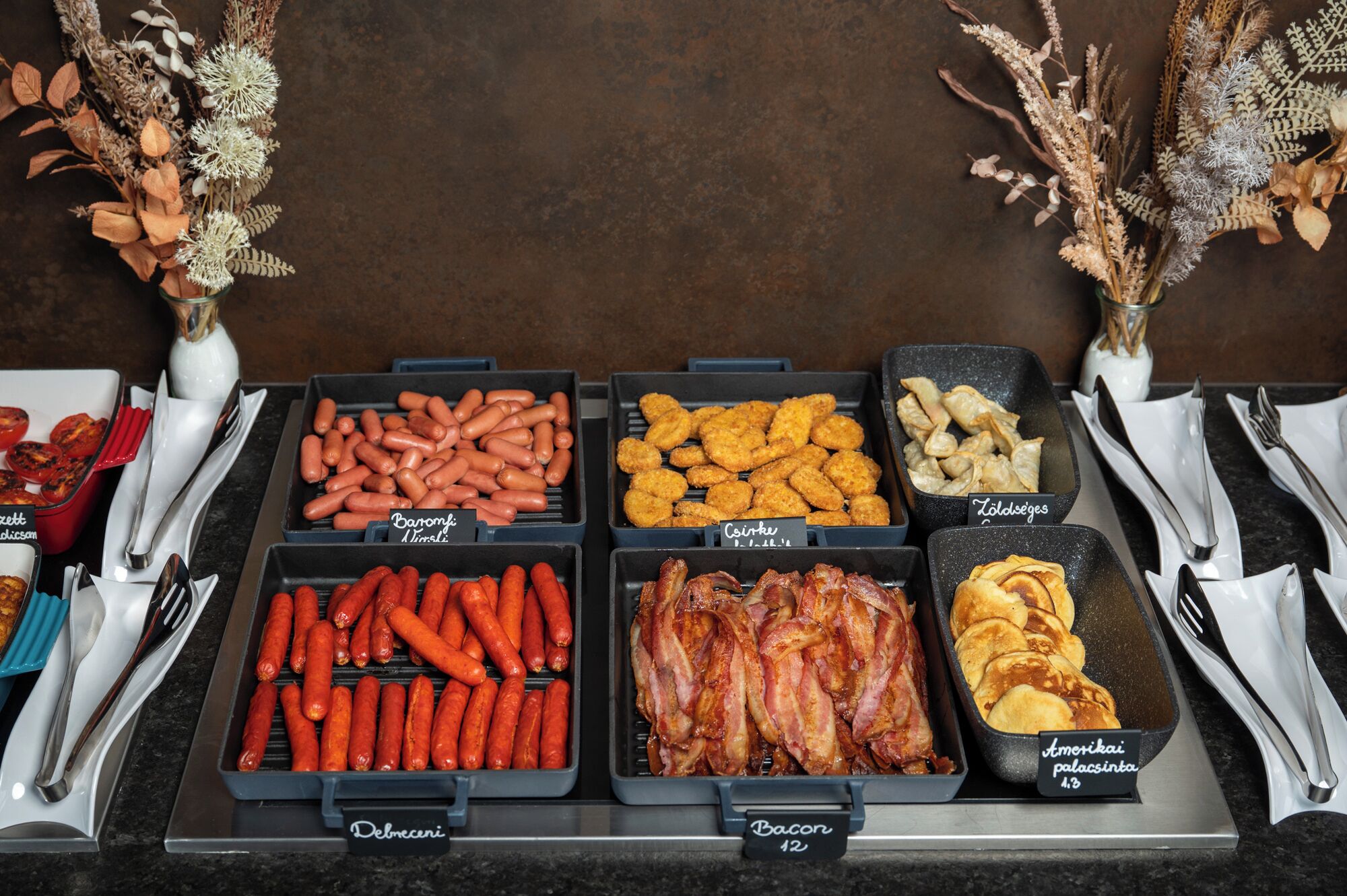 A buffet with various food options including sausages, bacon, and pastries.