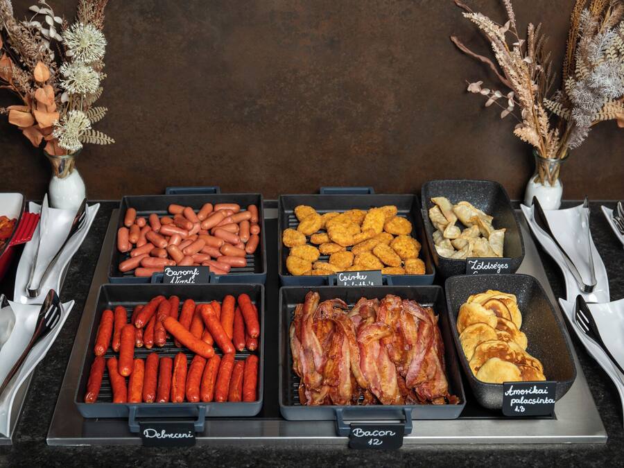 A buffet with various food options including sausages, bacon, and pastries.
