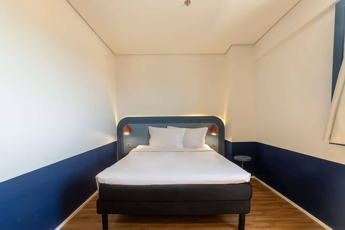A hotel room with a bed, a nightstand, and a wall-mounted lamp.