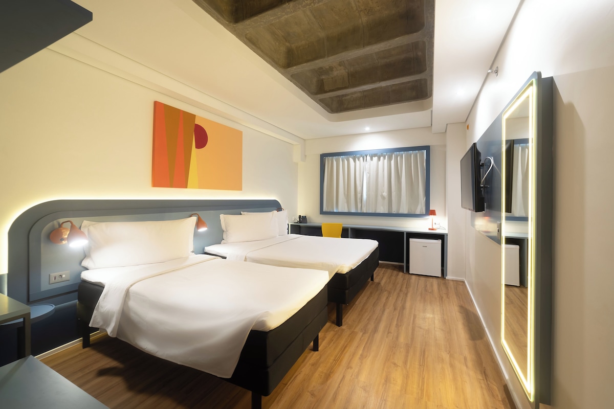 Camera d'albergo con due letti, una scrivania, una televisione e un bagno con doccia e servizi igienici.