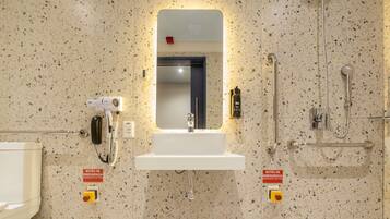 A bathroom with a sink, mirror, hand dryer, and a shower area.