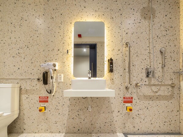 A bathroom with a sink, mirror, hand dryer, and a shower area. - Ibis Styles Fortaleza Giga Mall (Fortaleza)