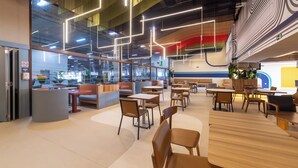 Una cafetería moderna con diversas opciones de asientos, incluyendo mesas, sillas, una barra y una cocina visible al fondo.