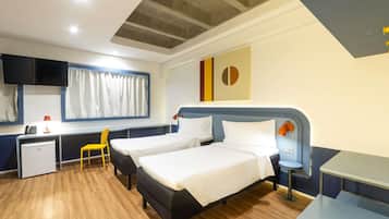 Habitació d'hotel amb dos llits, un escriptori, una cadira, un mini-frigorífic i una televisió.
