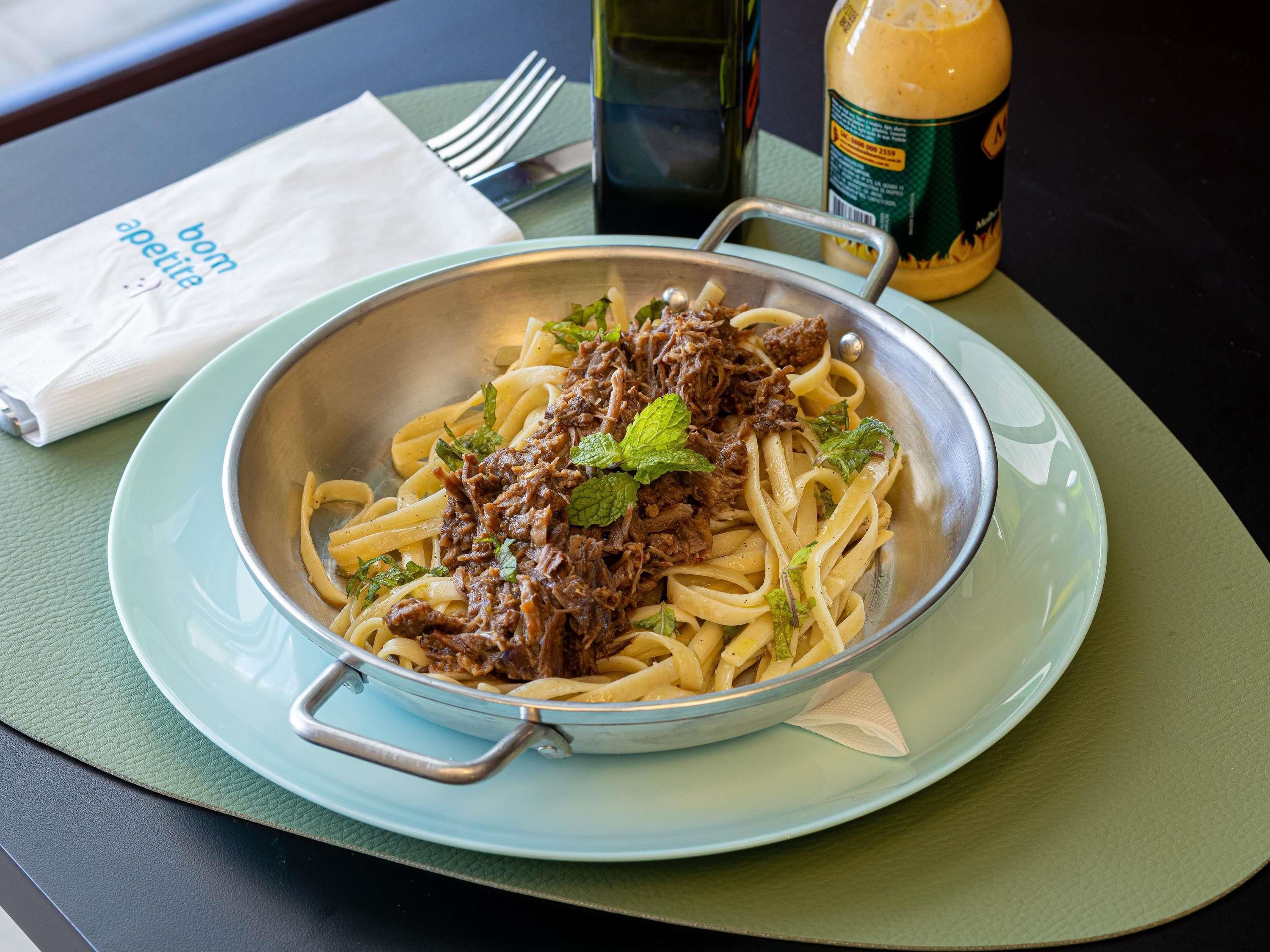 Un plato de pasta con carne y adorno de menta, junto a una botella de salsa y una servilleta.