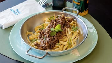 Un plato de pasta con carne y adorno de menta, junto a una botella de salsa y una servilleta.
