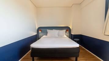 A hotel room with a bed, a nightstand, a lamp, and a wooden floor.
