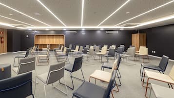 A conference room with a modern design, featuring a long table with chairs, a stage area, and a dark wall with a wooden panel.
