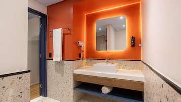 A modern bathroom with a white sink, a towel rack, a handheld hair dryer, and a mirror with an illuminated frame.