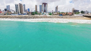 A coastal cityscape with a clear turquoise sea, a rocky shoreline, and a backdrop of modern high-rise buildings. - Ibis Styles Fortaleza Giga Mall (Fortaleza)