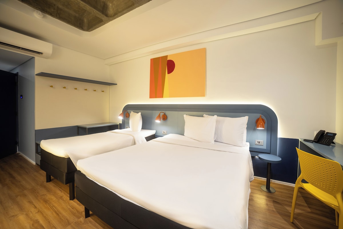 A hotel room with two beds, a desk, a chair, and a wall-mounted artwork.